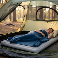 Person lying in a camping tent with a blue blanket in a forest setting